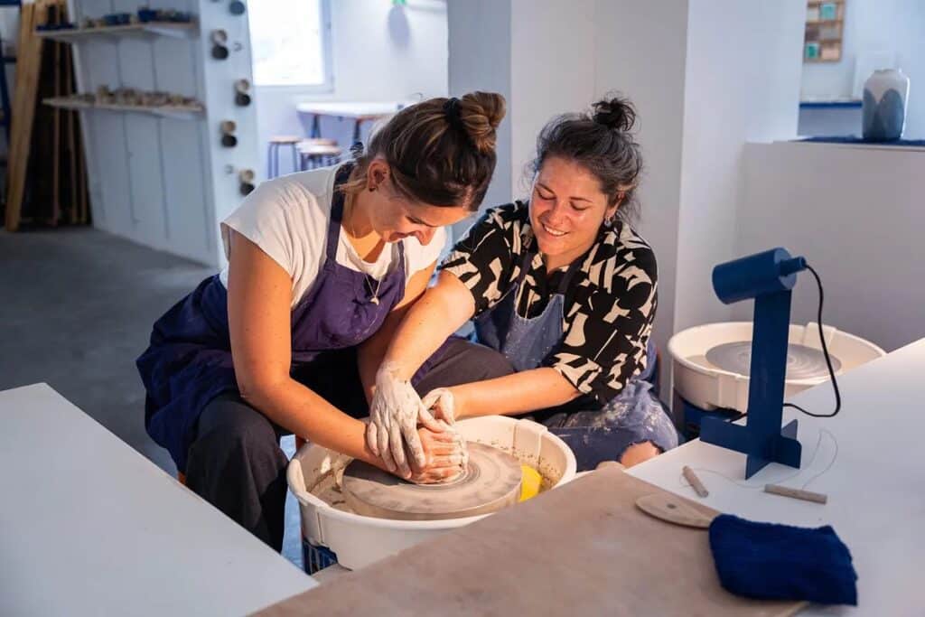 Une formatrice apprend à une stagiaire le tournage en céramique dans un atelier de poterie.