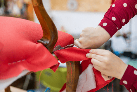 Mains utilisant une agrafeuse pour fixer un tissu orange sur une assise.