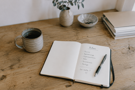 Carnet ouvert et tasse en céramique sur une table en bois dans une ambiance calme et artisanale.